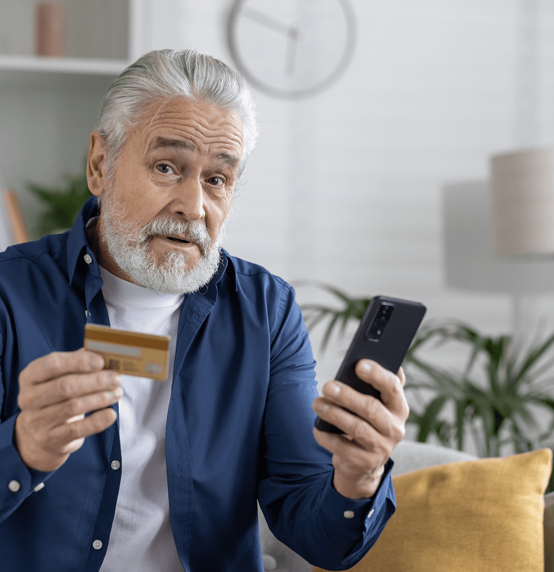 Man holding credit card and smartphone indoors.